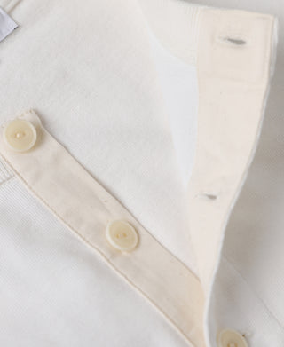 Close-up of a cream-colored knit garment, showing a buttoned placket with matching cream buttons and a soft textured fabric.
