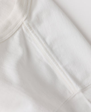 Close-up detail of a white ribbed knit garment, showing the texture of the fabric and the construction of the collar and sleeve seam.