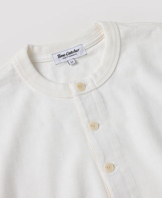 Close-up of a white Henley shirt by Time Catcher, showing the ribbed crew neck, three cream buttons, and the brand label inside the collar.