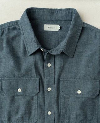 Blue flannel work shirt front view, collar with white buttons and two buttoned chest pockets.