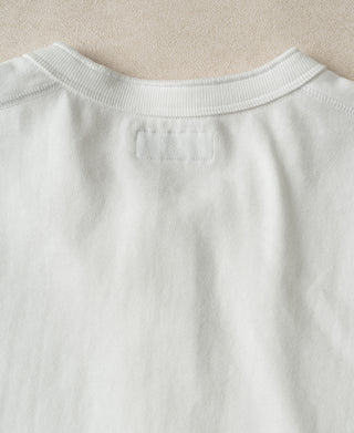 Close-up of the back collar of a white crewneck sweatshirt, showing a blank rectangular patch for branding on the back neck, set against a neutral beige textured background.