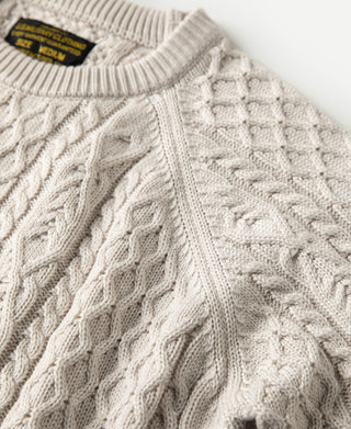 Cream cable knit sweater shoulder with black logo tag on collar