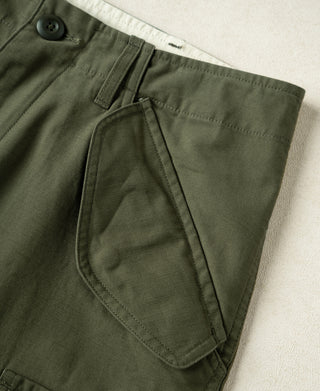 Olive trouser front with pocket seams, rounded flap, and button closure