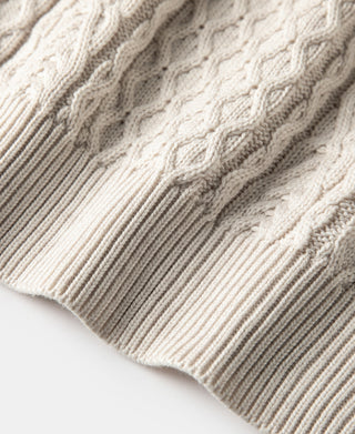 Close-up of cream sweater knit with cable bands and ribbed hem
