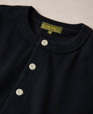 Close-up of a black garment with white buttons and a visible brand label on a beige background
