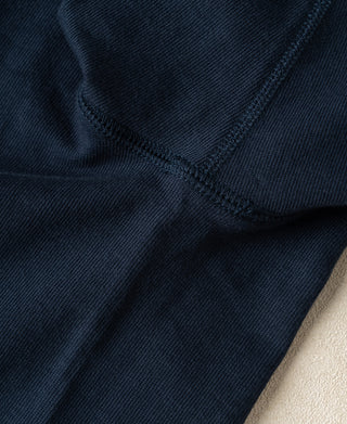 Close-up of dark navy blue ribbed knit fabric with a diagonal seam and a small area of light beige material at the bottom right.