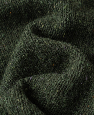 Close-up view of the chunky knit texture and natural speckled wool fibers on a dark green sweater.